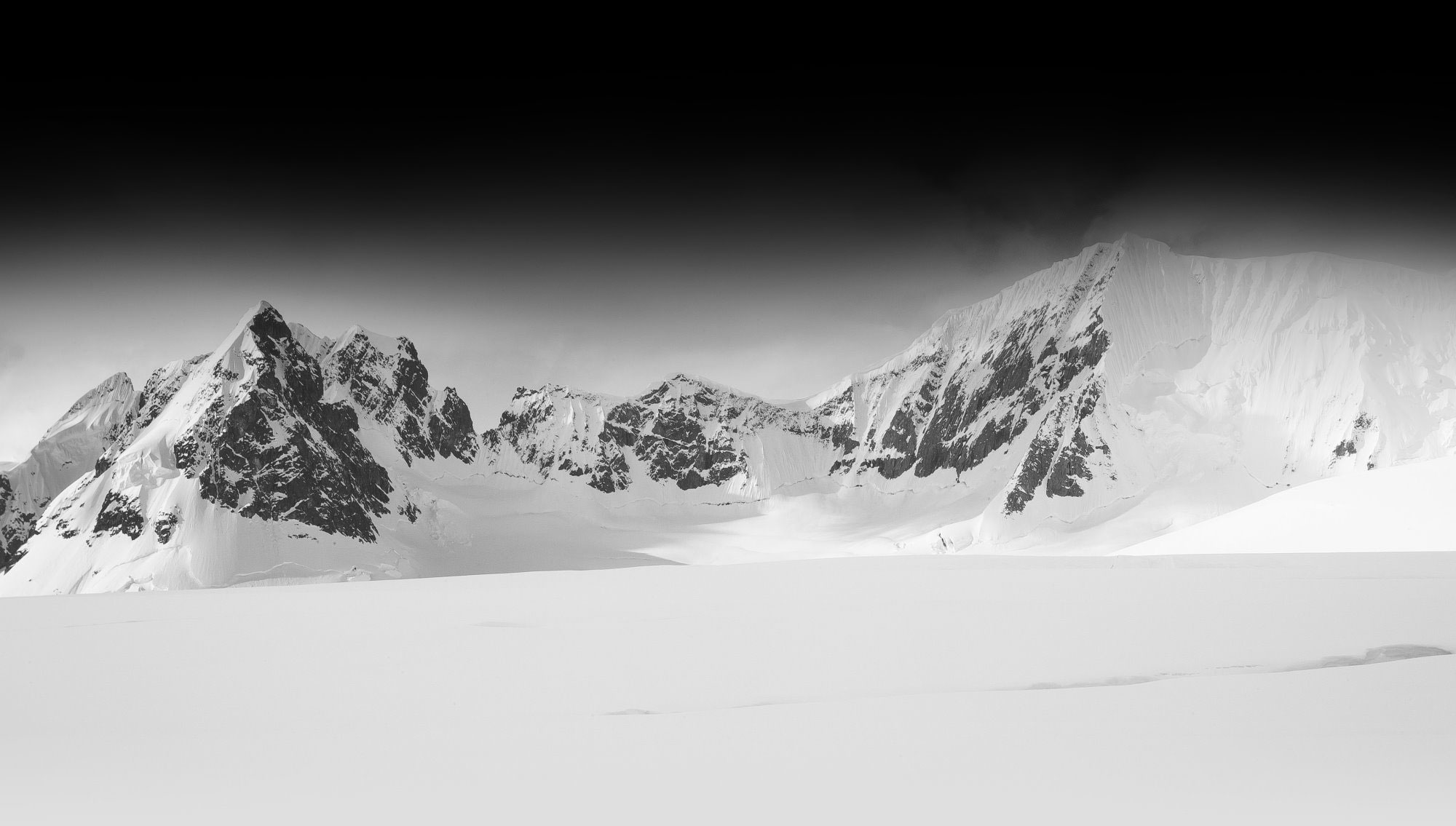 Elegante snødekte fjell i svart-hvitt, som skaper en tidløs og dramatisk atmosfære i vinterlandskapet.