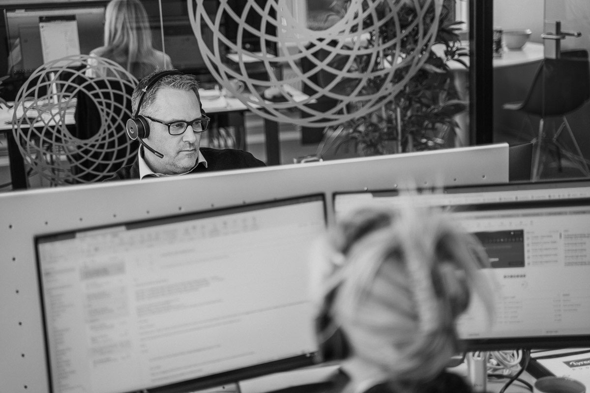 En mann med headset arbeider konsentrert ved datamaskinen, omgitt av en moderne og stilren arbeidsplass.