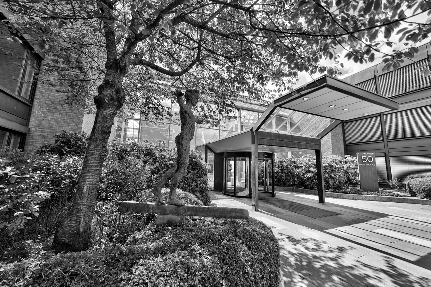 Svart-hvitt bilde av en storslått bygning omkranset av frodige trær og busker, som skaper en tidløs atmosfære.