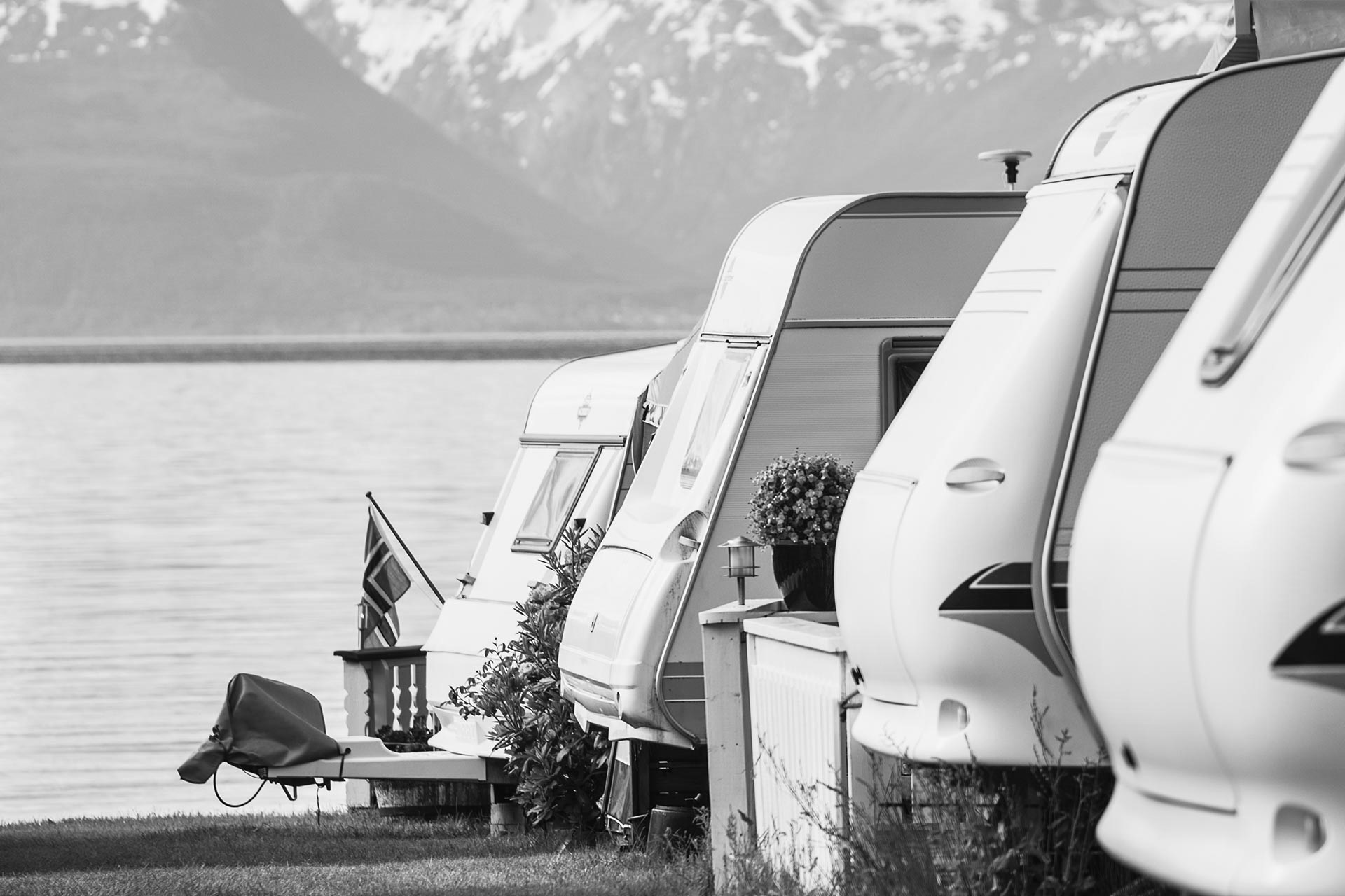 Svart-hvitt bilde av campingbiler parkert ved vannkanten, omfavnet av naturens ro og skjønnhet.