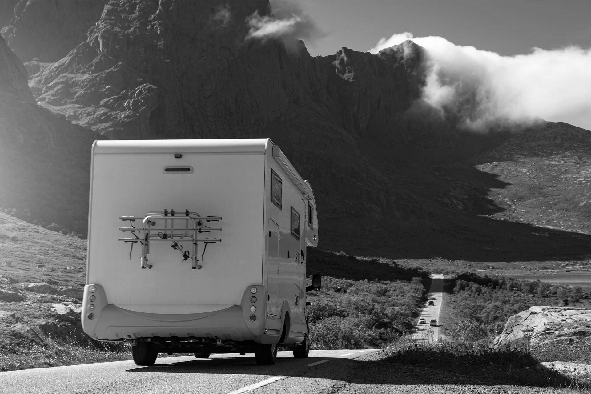 Et svart-hvitt bilde av en campervan som elegant kjører langs en stille vei, omfavnet av naturens ro.