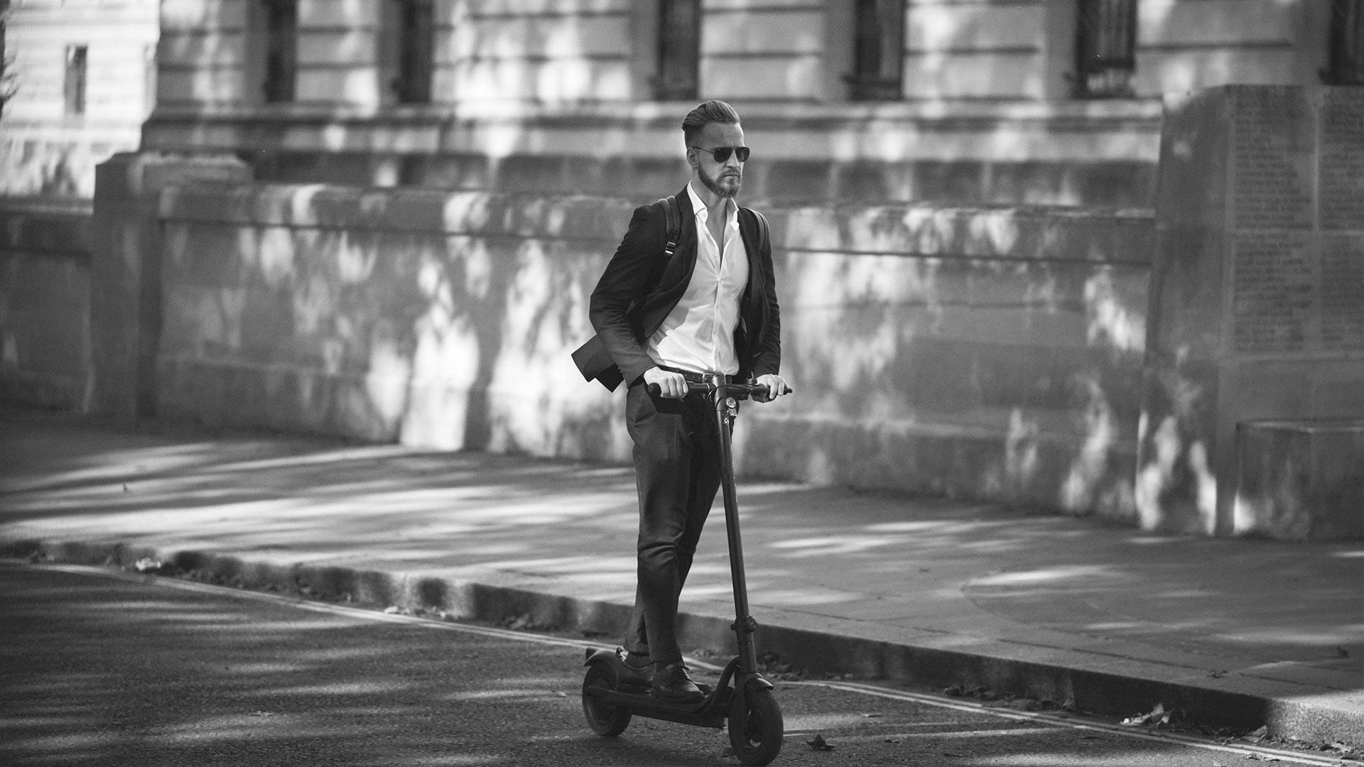 En stilfull mann iført dress suser forbi på en elektrisk scooter, en moderne reiseopplevelse.