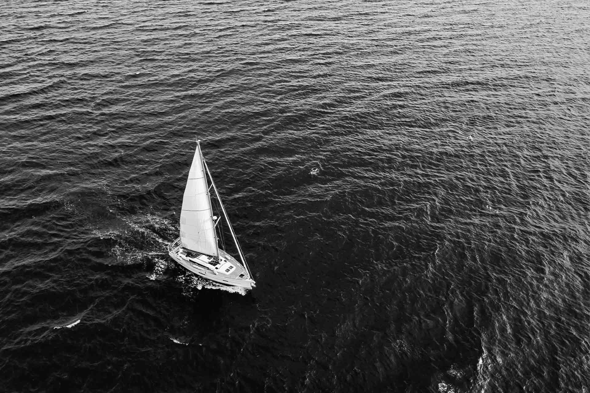 Luftbilde av en seilbåt som glir elegant over det glitrende havet, omfavnet av bølger og sollys.